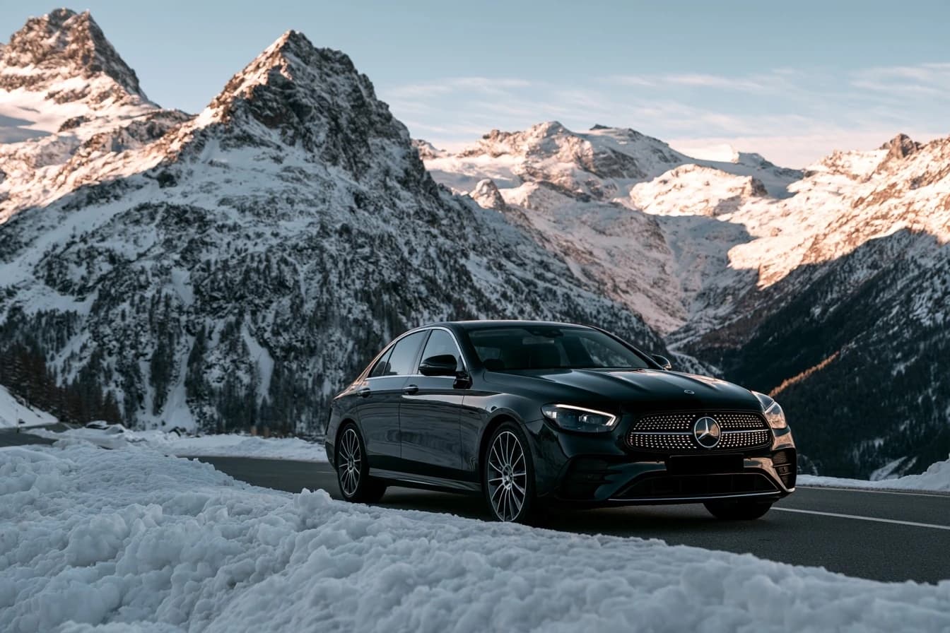 Black Mercedes E-Class sedan on an alpine road between snowy mountains in winter